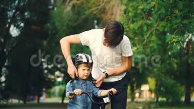 <strong>关爱</strong>的父亲在他的小儿子头上戴着安全帽`然后教导快乐的男孩在爱的同时骑自行车